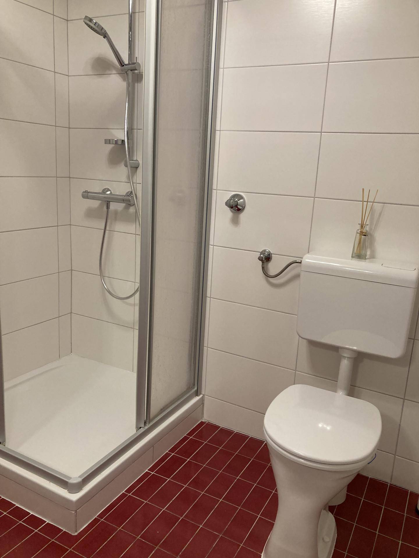 Funktionales Badezimmer mit Duschkabine, WC und roten Bodenfliesen.