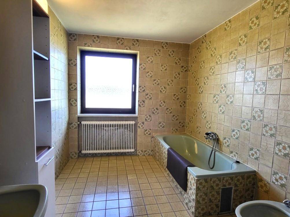 Badezimmer im 80er-Jahre-Stil mit gemusterten Fliesen, Badewanne und Fenster.