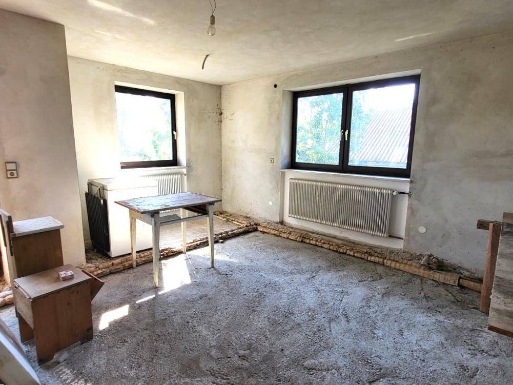 Unfertiger Raum mit Betonboden und zwei Fenstern, bereit für den Ausbau.