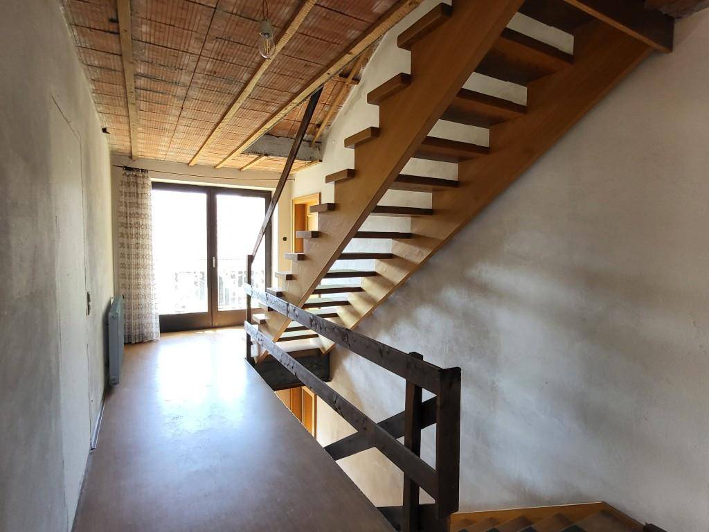 Treppenhaus mit Holztreppe, unverputzter Decke und Zugang zu einem Balkon.