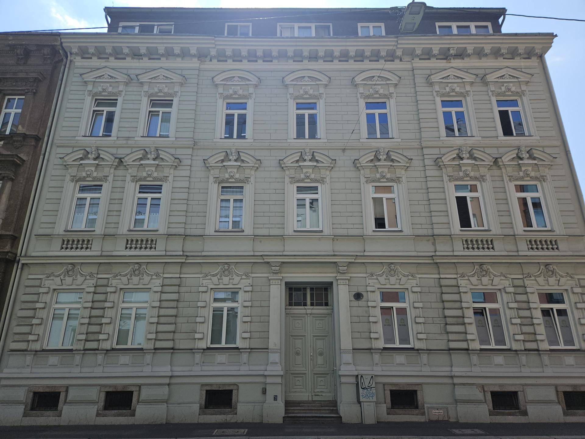 Historische Fassade eines Mehrfamilienhauses mit vielen Fenstern und dekorativen Elementen.