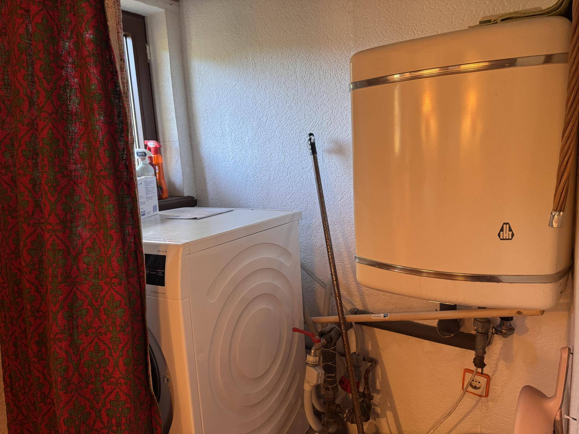 Praktischer Hauswirtschaftsraum mit Waschmaschine und Warmwasserboiler, gut organisiert.