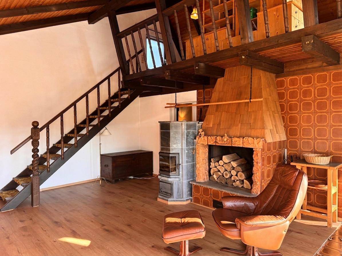 Geräumiges Wohnzimmer mit Holzbalken, Kamin und Treppe zur Galerie, strahlt rustikalen Charme aus.