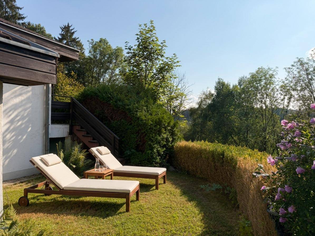 Sonnige Rasenfläche mit Liegestühlen und Hecke, umgeben von üppiger Vegetation und Bäumen.