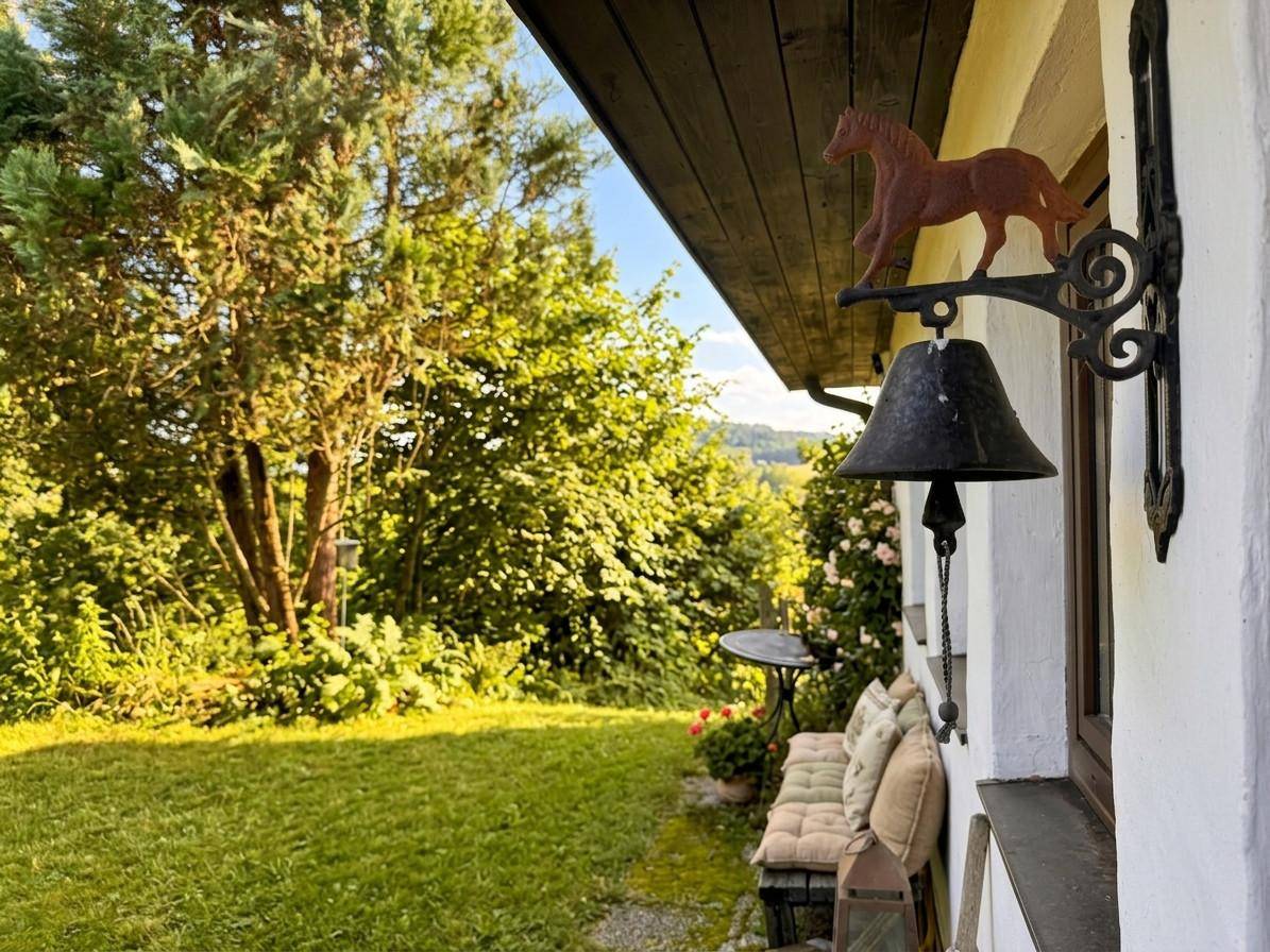 Kleiner Gartenbereich neben dem Haus mit einer Bank und einer dekorativen Glocke an der Wand.