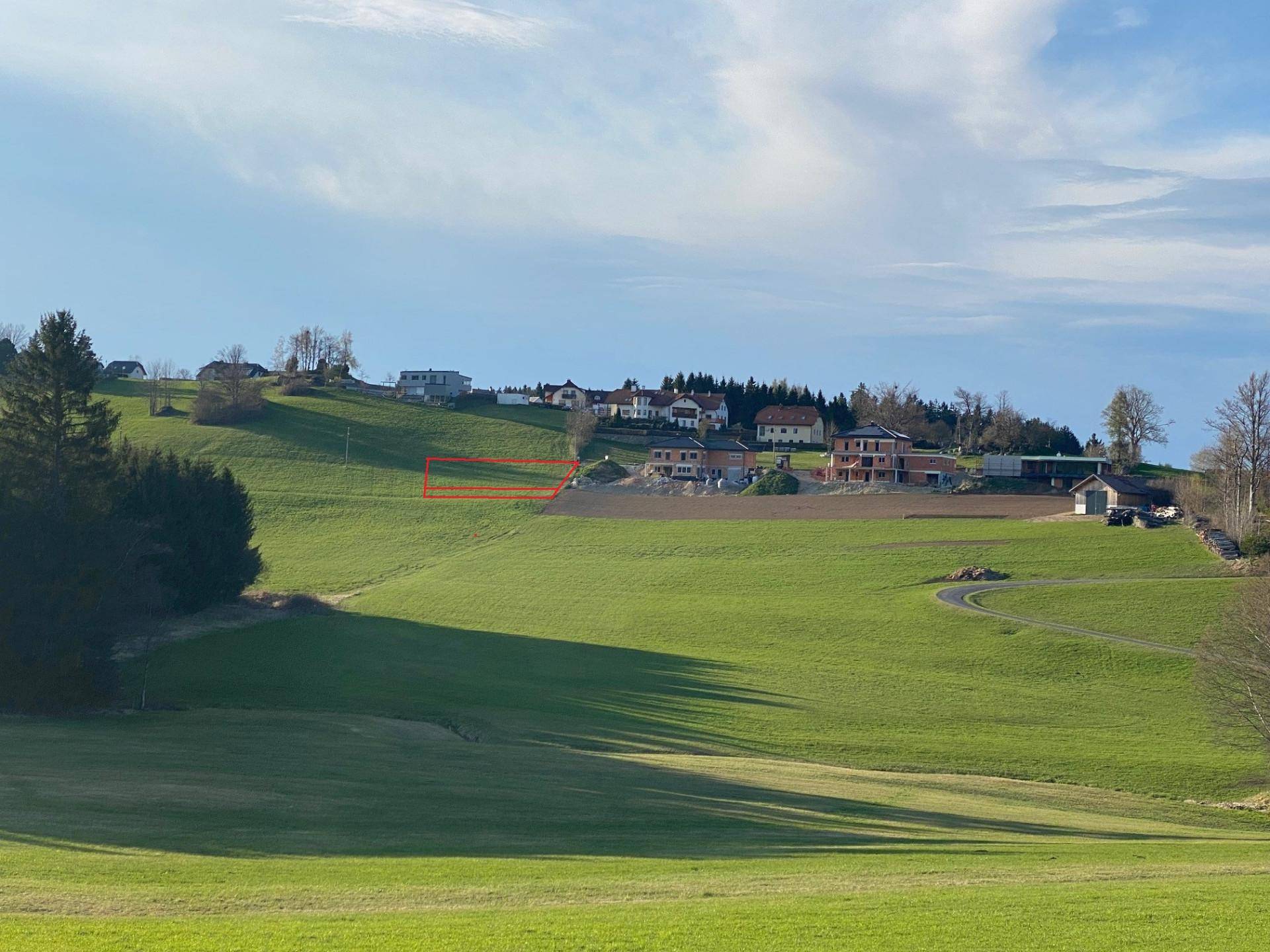 Grüne Hügellandschaft mit Häusern in der Ferne und einem markierten Grundstück.