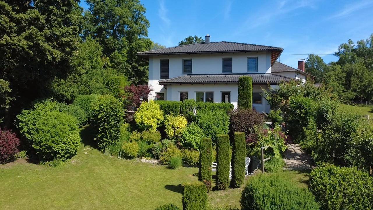 Das Haus eingebettet in eine üppige, grüne Gartenlandschaft unter einem klaren blauen Himmel.