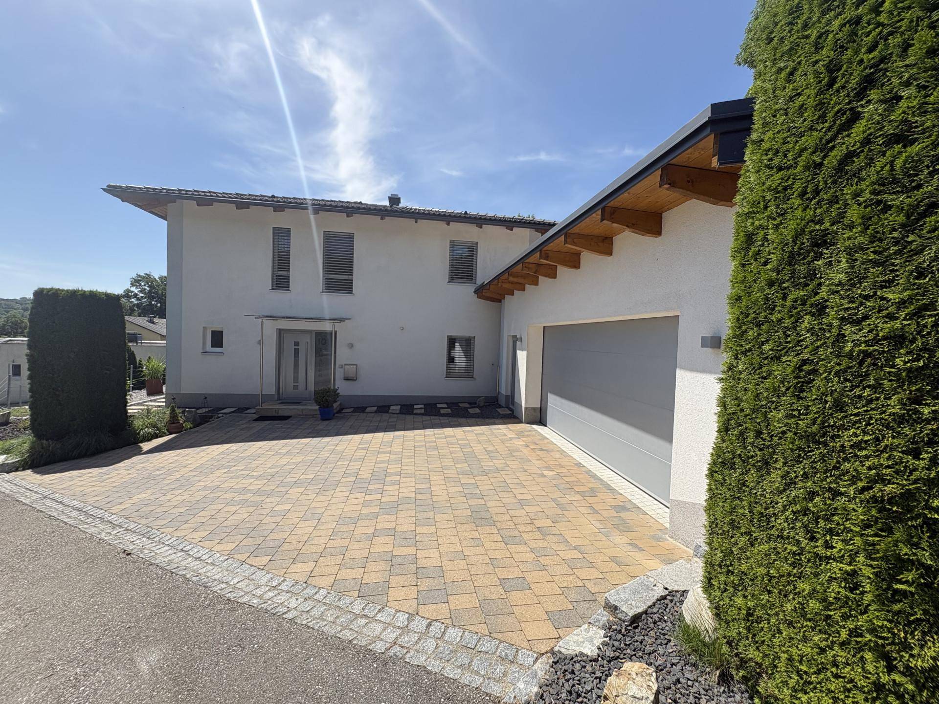 Moderne Hausfassade mit gepflasterter Auffahrt und integrierter Garage unter strahlendem Sonnenschein.