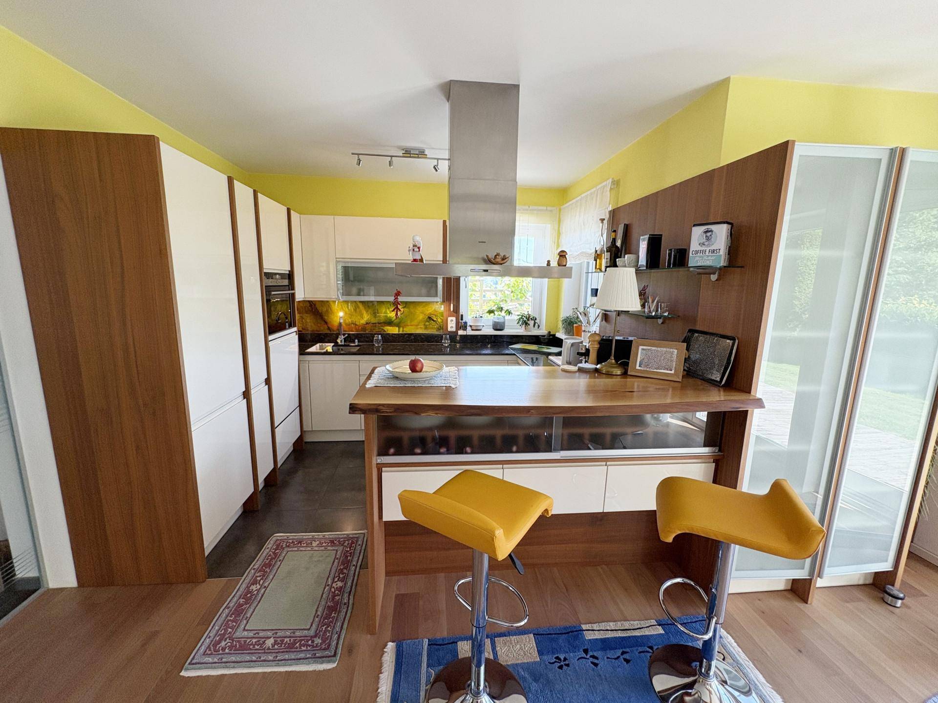 Moderne Küche mit Holzelementen, weißen Hochglanzfronten und einer Kücheninsel mit gelben Barhockern.