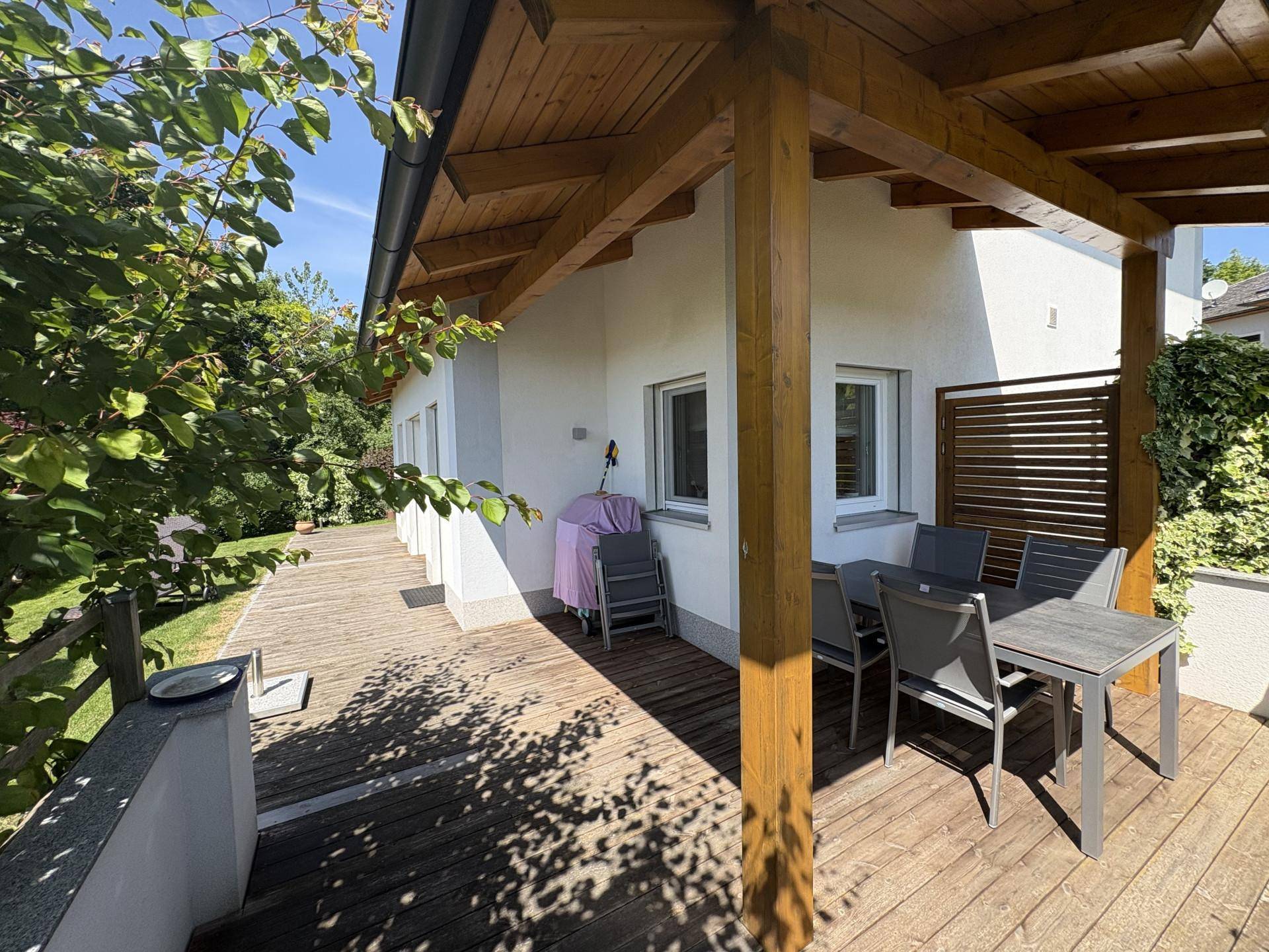 Überdachte Holzterrasse mit Esstisch und Stühlen, ideal für Mahlzeiten im Freien.