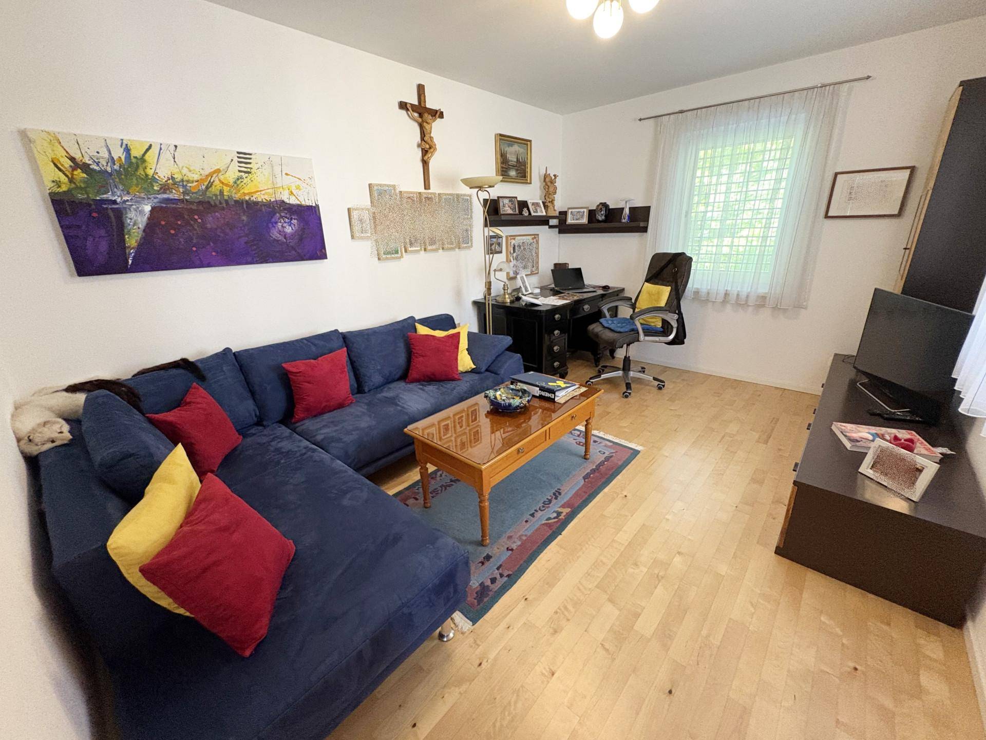 Arbeitszimmer mit blauem Ecksofa, Schreibtisch und hellem Holzboden, ideal für Home-Office oder Gäste.