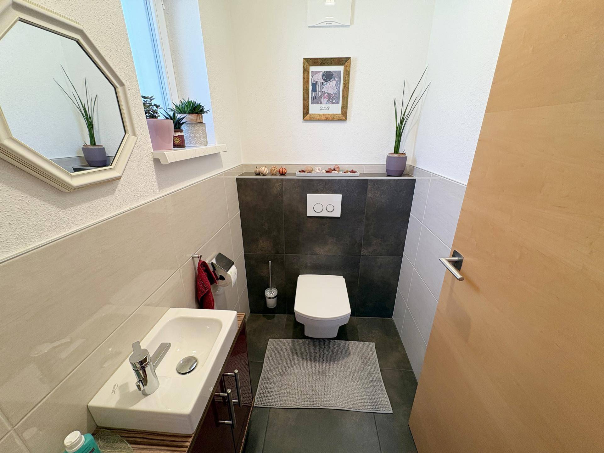 Modernes Gäste-WC mit wandhängender Toilette und kleinem Waschbecken in neutralen Fliesen.