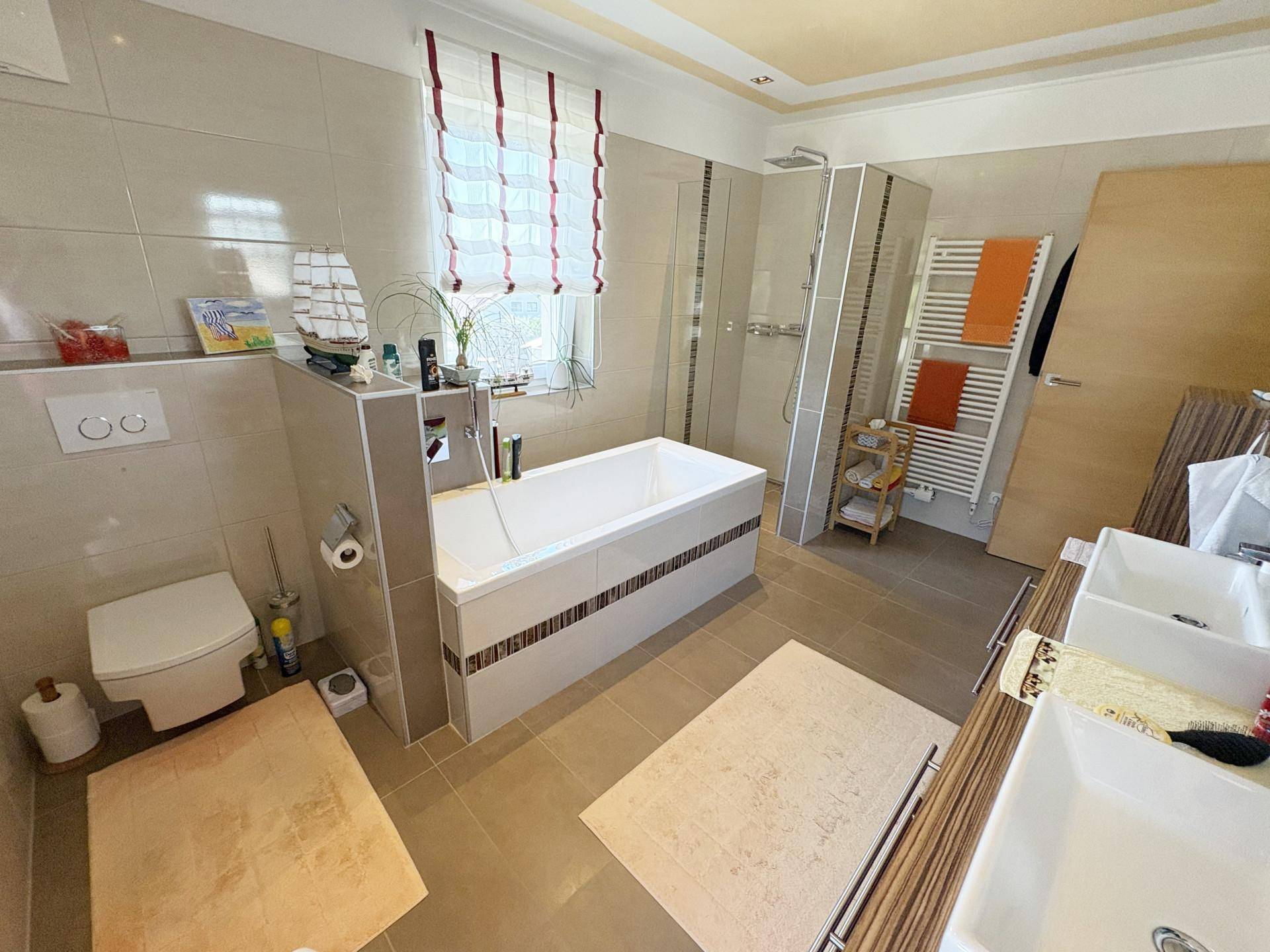 Modernes Badezimmer mit Badewanne, ebenerdiger Dusche, WC und Doppelwaschbecken in hellen Fliesen.