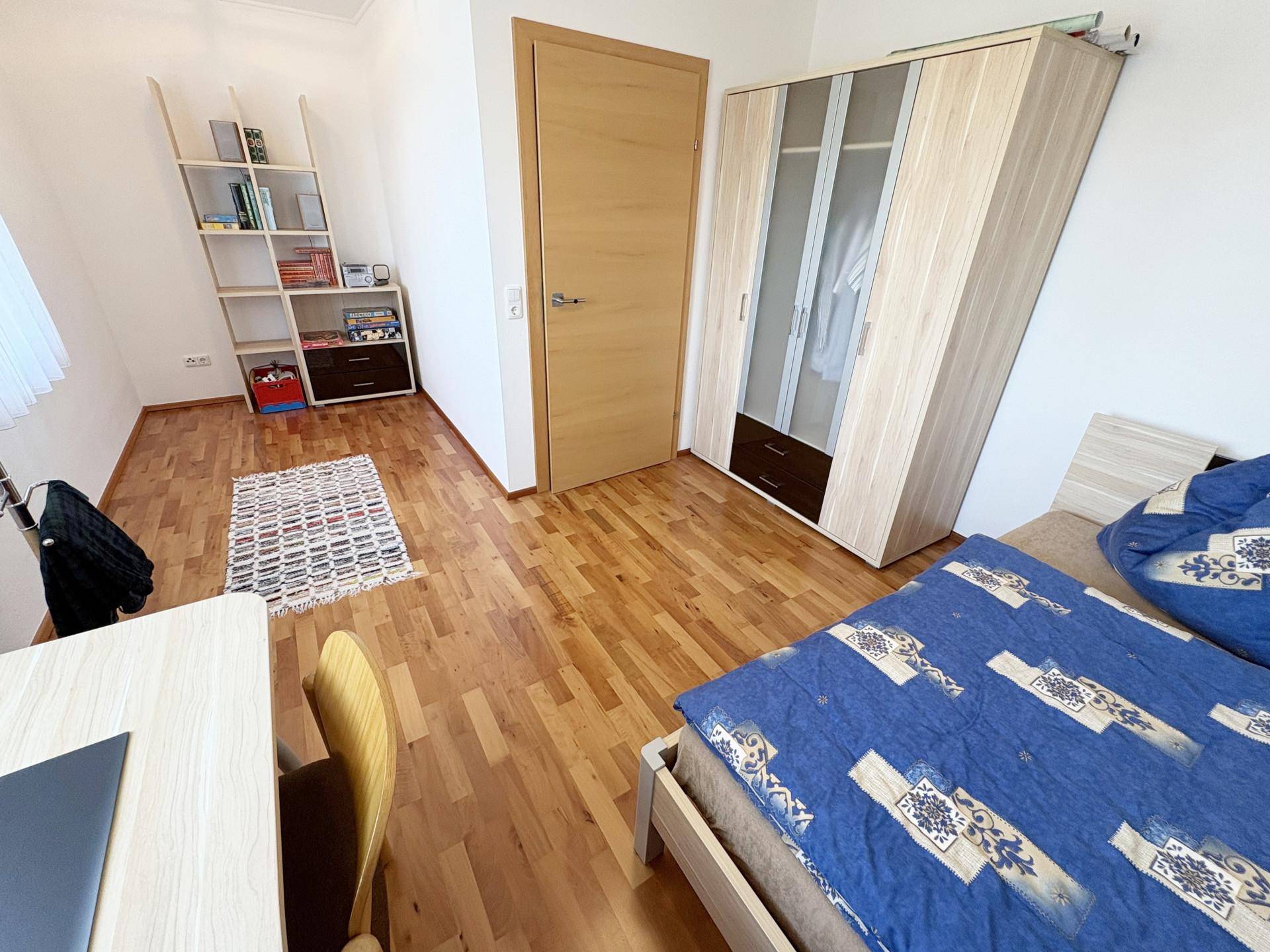 Helles Schlafzimmer mit Einzelbett, Kleiderschrank und Schreibtisch, ausgestattet mit Holzboden.