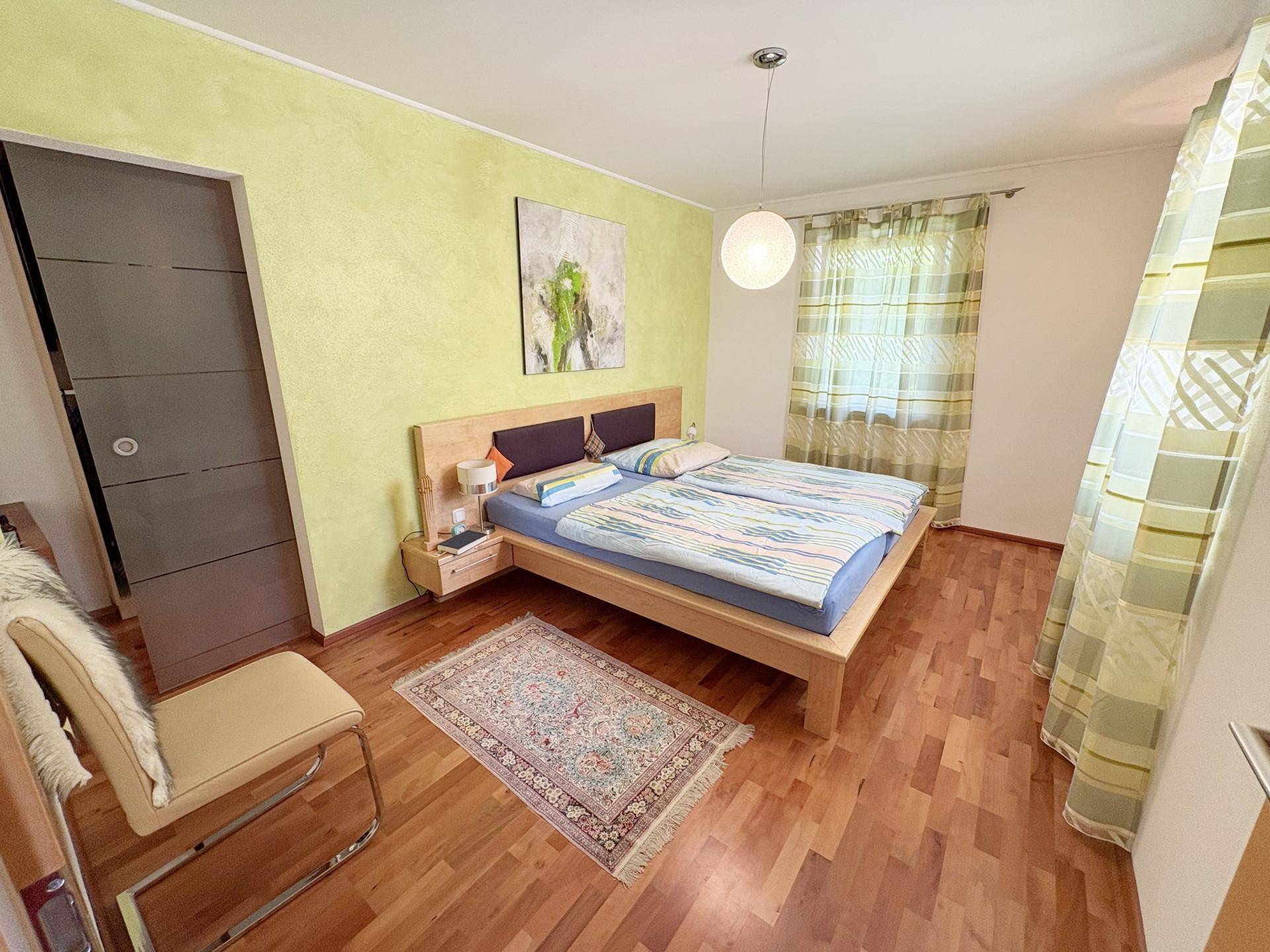 Schlafzimmer mit hellem Holzbett, grüner Akzentwand und warmem Holzboden, bietet eine ruhige Atmosphäre.