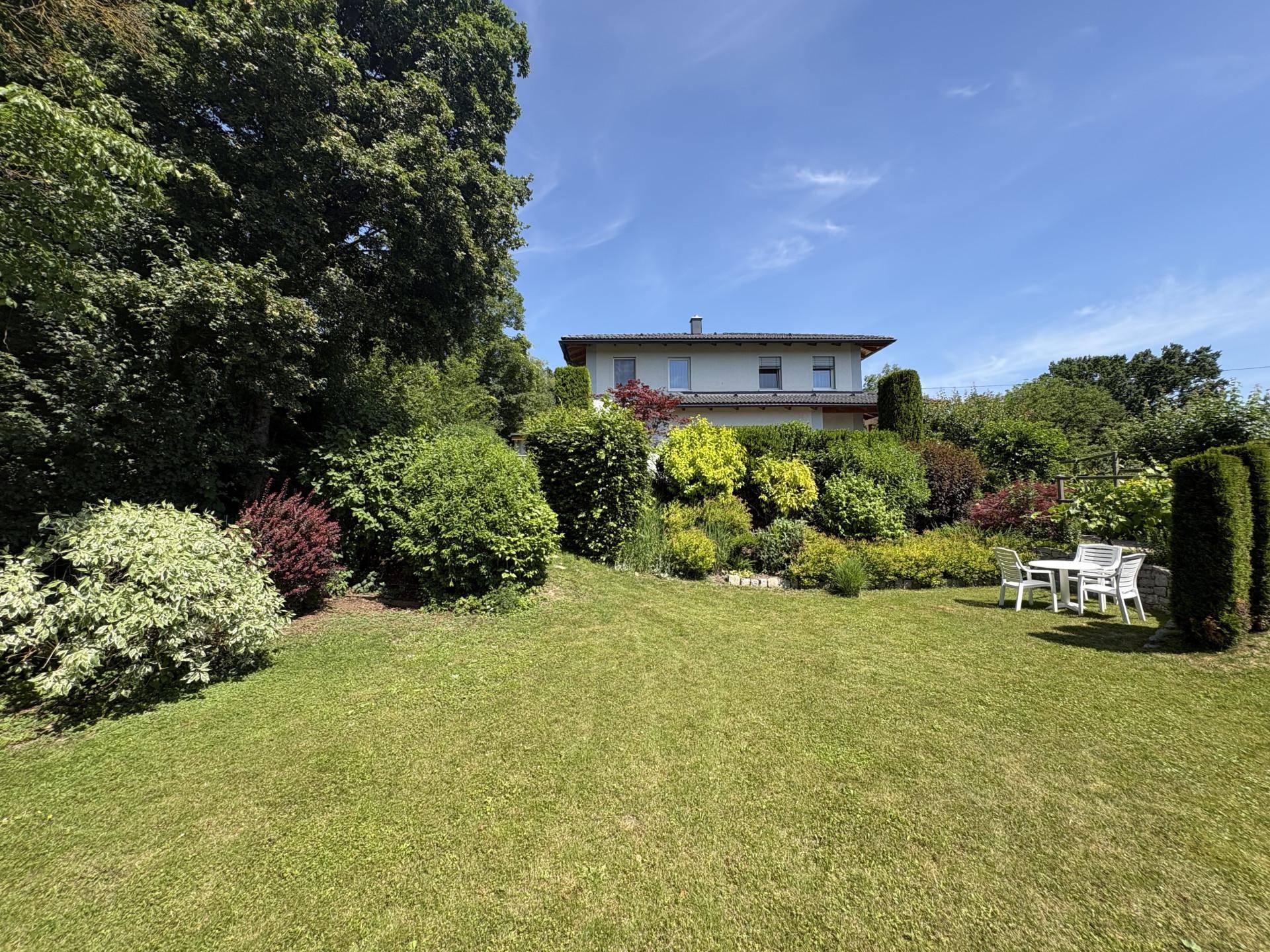 Weitläufiger Garten mit Rasenfläche, vielfältiger Bepflanzung und einer Sitzgruppe im Freien.