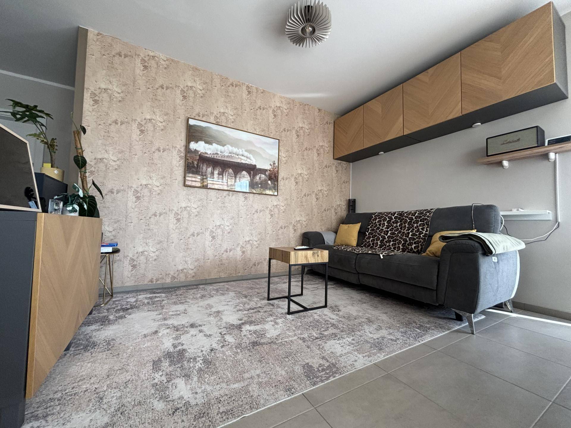 Gemütliches Wohnzimmer mit strukturierter Tapete, modernem Teppich und schwebenden Holzmöbeln.