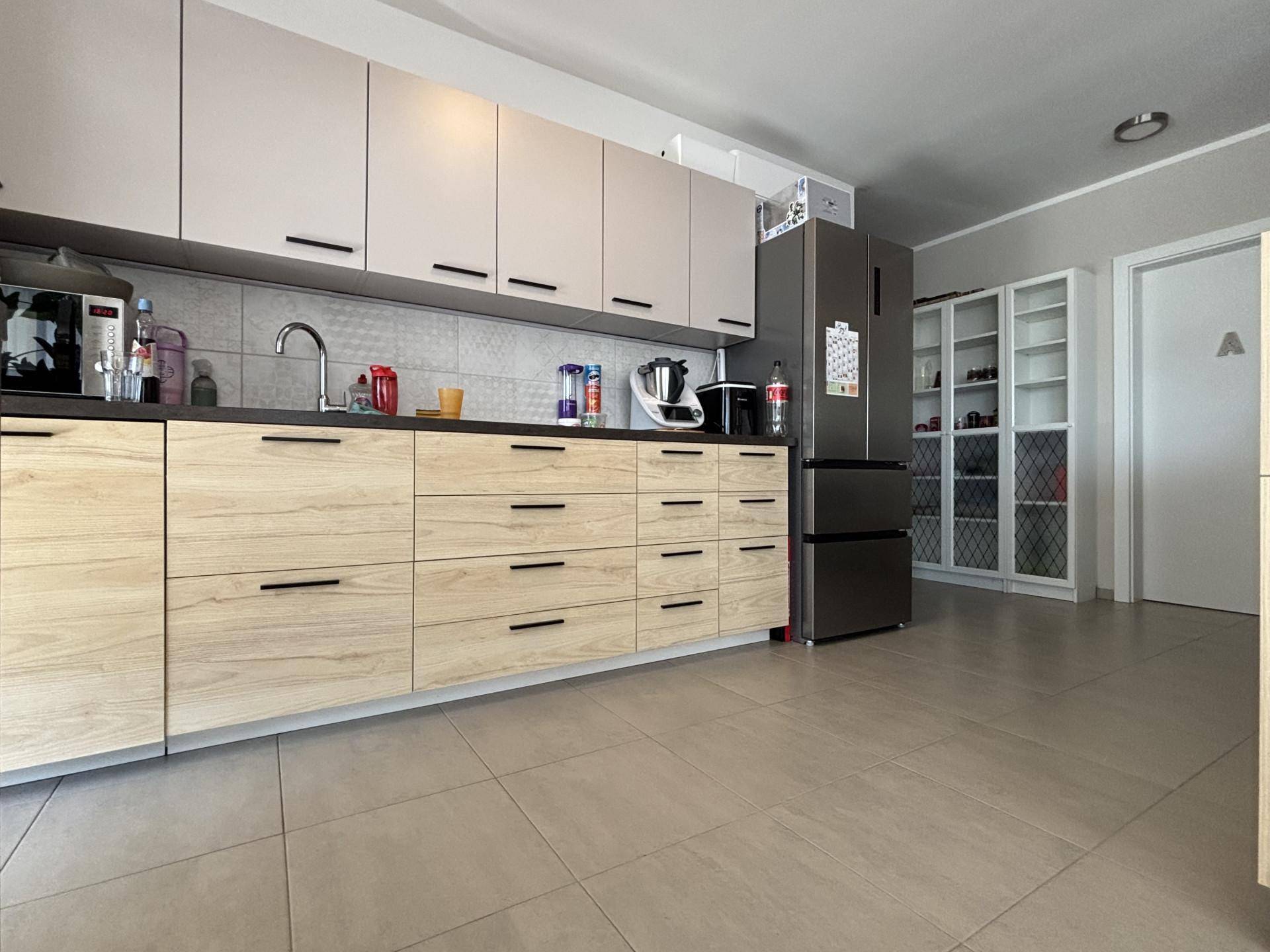 Moderne Küche mit hellen Holzfronten, grauen Oberschränken und Fliesenboden, inklusive Kühlschrank.