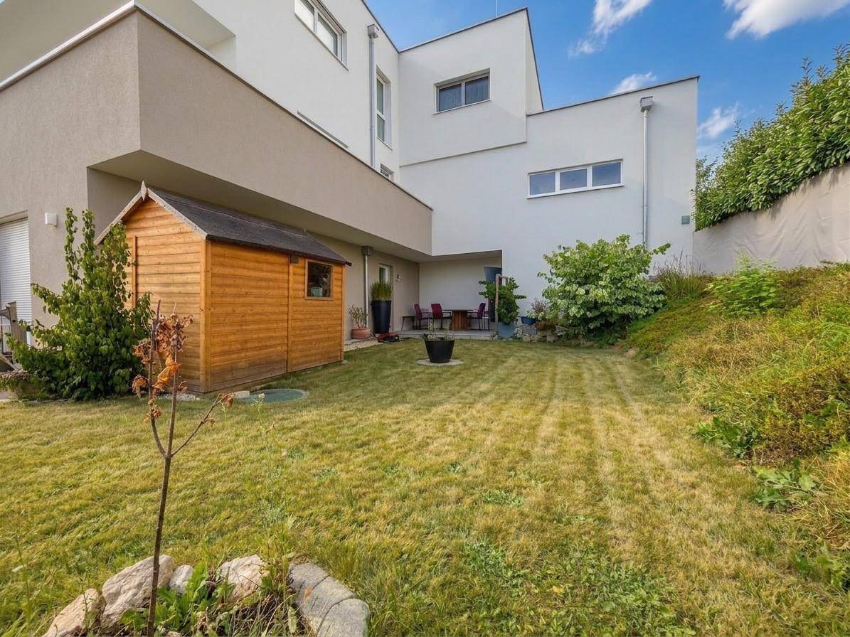 Hinterhof mit einem kleinen Holzschuppen und einer Rasenfläche, umgeben von viel Grün.