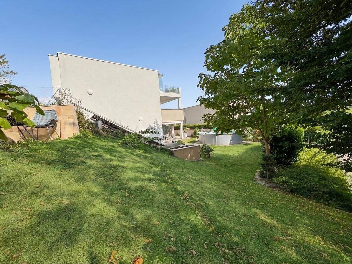 Großer, abfallender Gartenbereich mit altem Baum und Blick auf die moderne Architektur des Hauses.