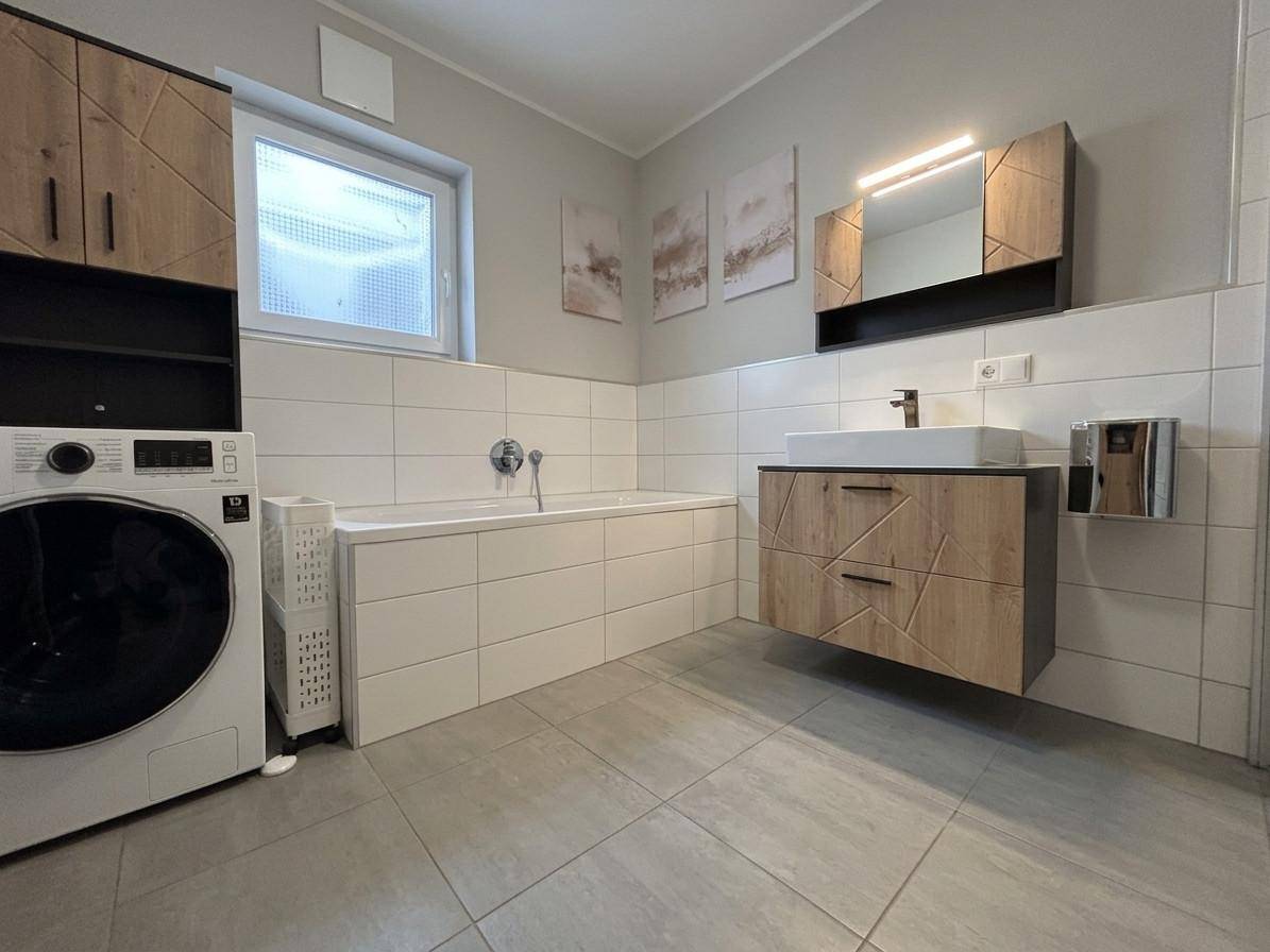 Modernes Badezimmer mit Badewanne, Waschbecken und Waschmaschine, hell gefliest und funktional.