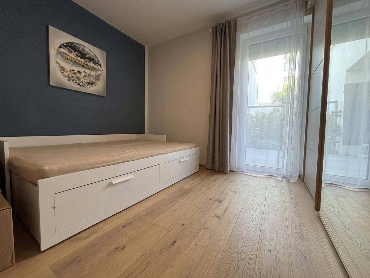 Schlafzimmer mit Holzboden, blauer Akzentwand und Zugang zu einem Balkon durch große Fenster.