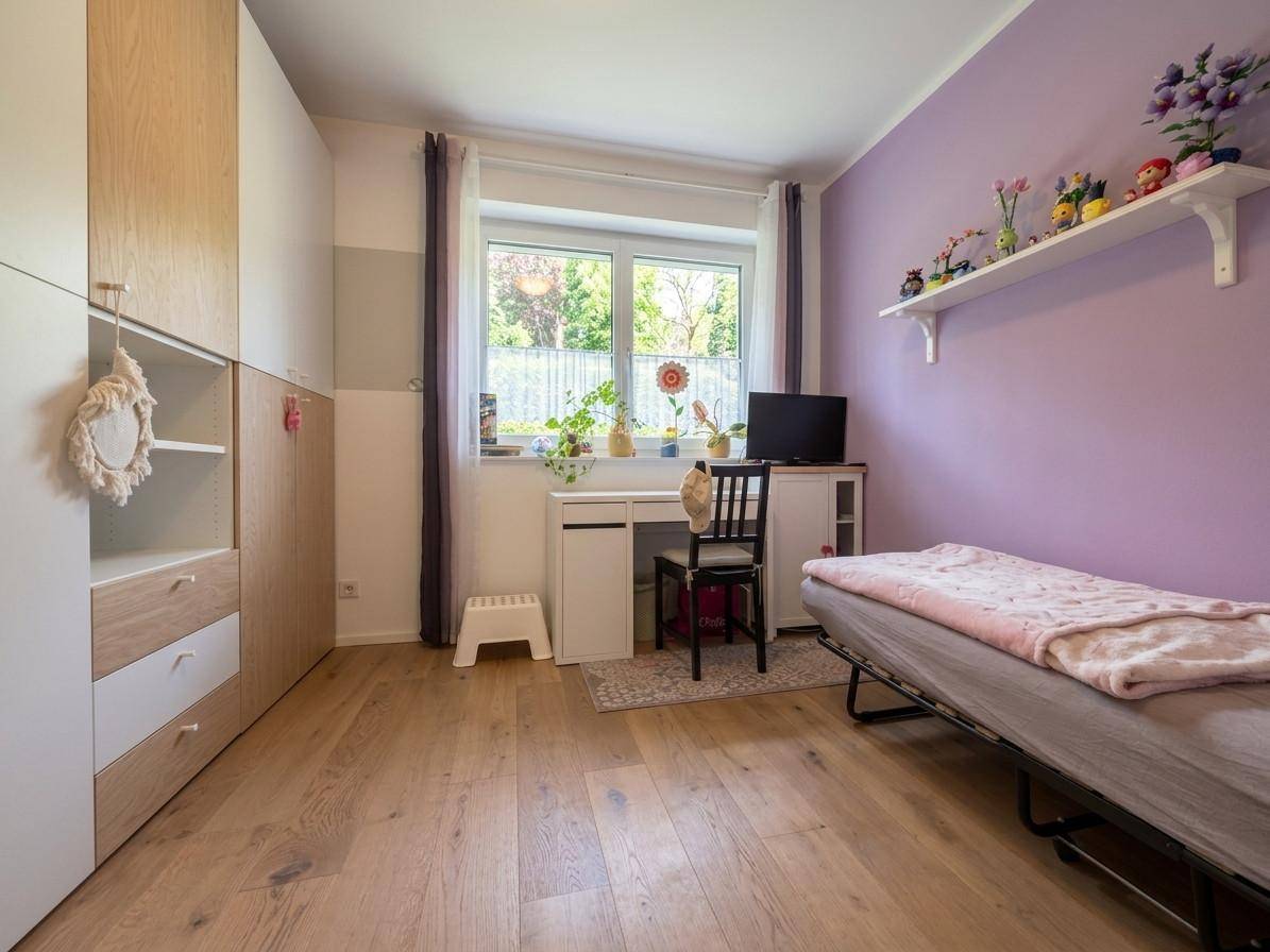 Kinderzimmer mit Holzboden, lila Wand und Fenster mit Blick ins Grüne, hell und freundlich.