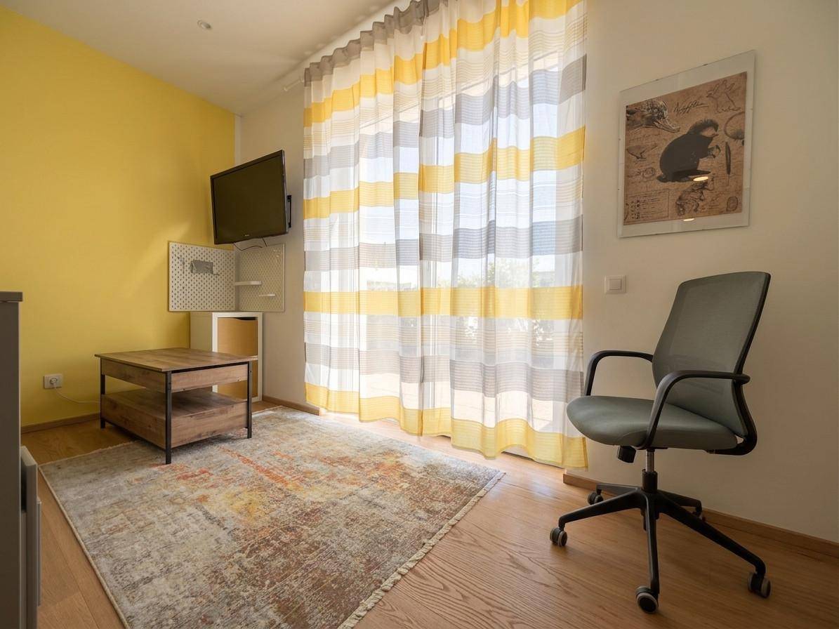 Helles Arbeitszimmer mit gelber Akzentwand, Holzboden und großem Fenster für viel Tageslicht.