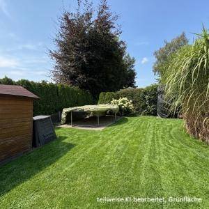 Gepflegter Garten mit Rasenfläche, hohen Hecken und einem kleinen Gartenhaus.