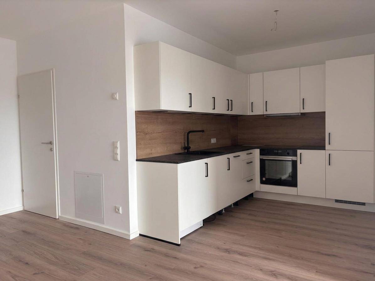 Moderne Einbauküche mit weißen Schränken, dunkler Arbeitsplatte und integriertem Backofen.