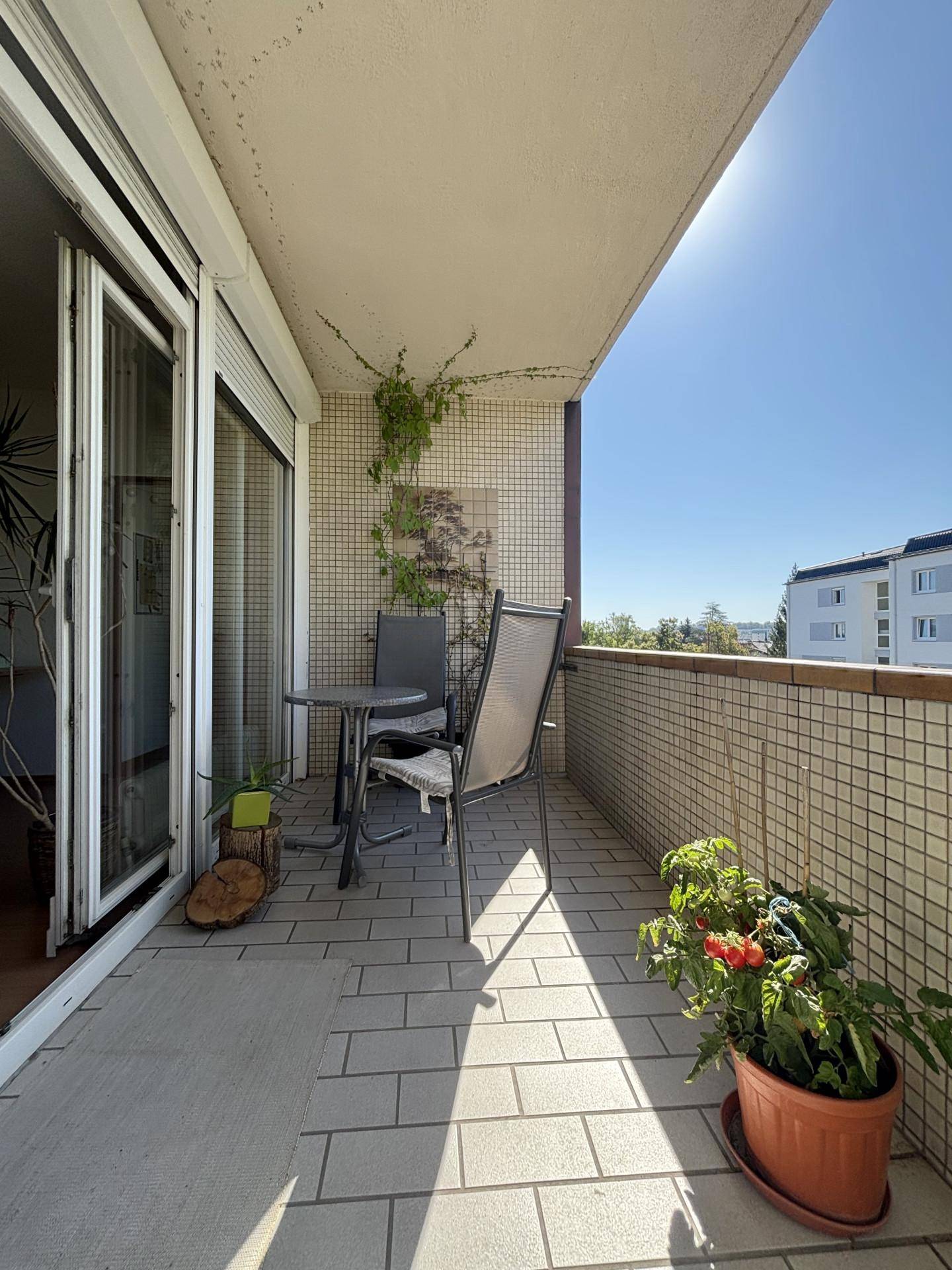 Sonniger Balkon mit Fliesenboden, Sitzgelegenheiten und Blick auf die Umgebung.