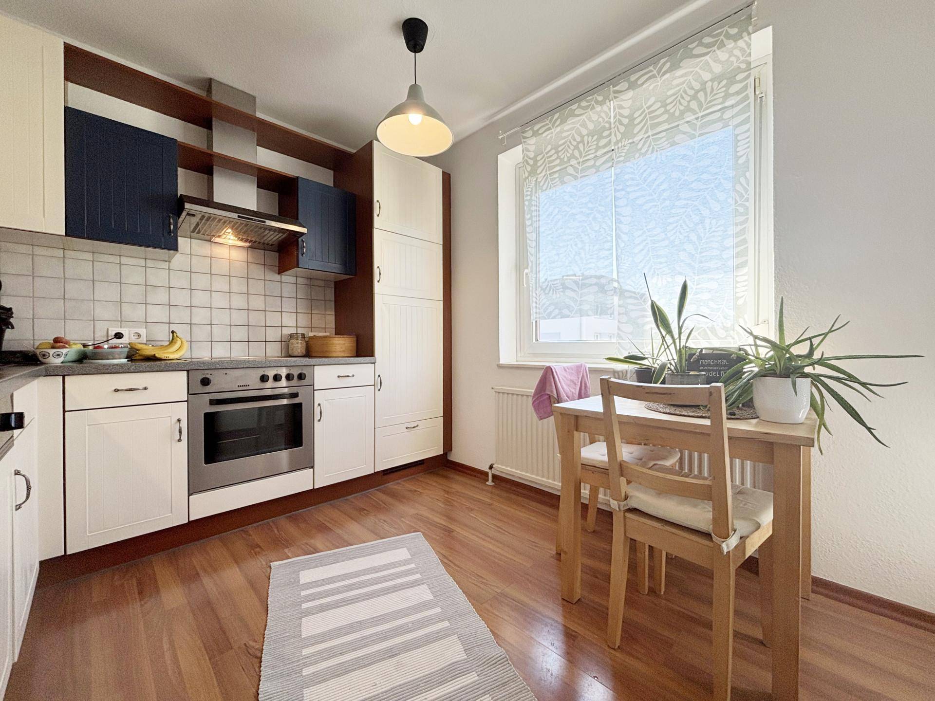 Funktionale Küche mit hellen Schränken, integriertem Backofen und kleinem Essbereich am Fenster.