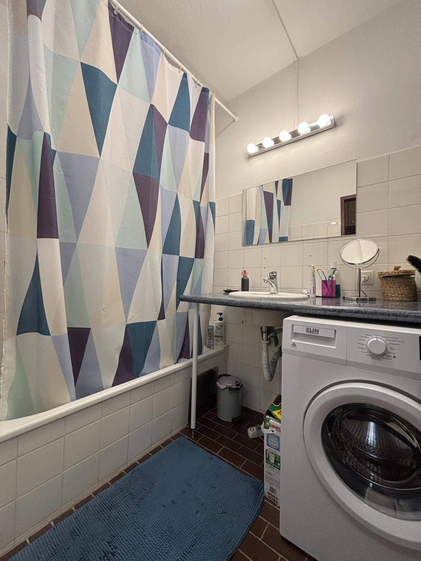 Badezimmer mit Badewanne, Waschbecken, Spiegel und integrierter Waschmaschine.