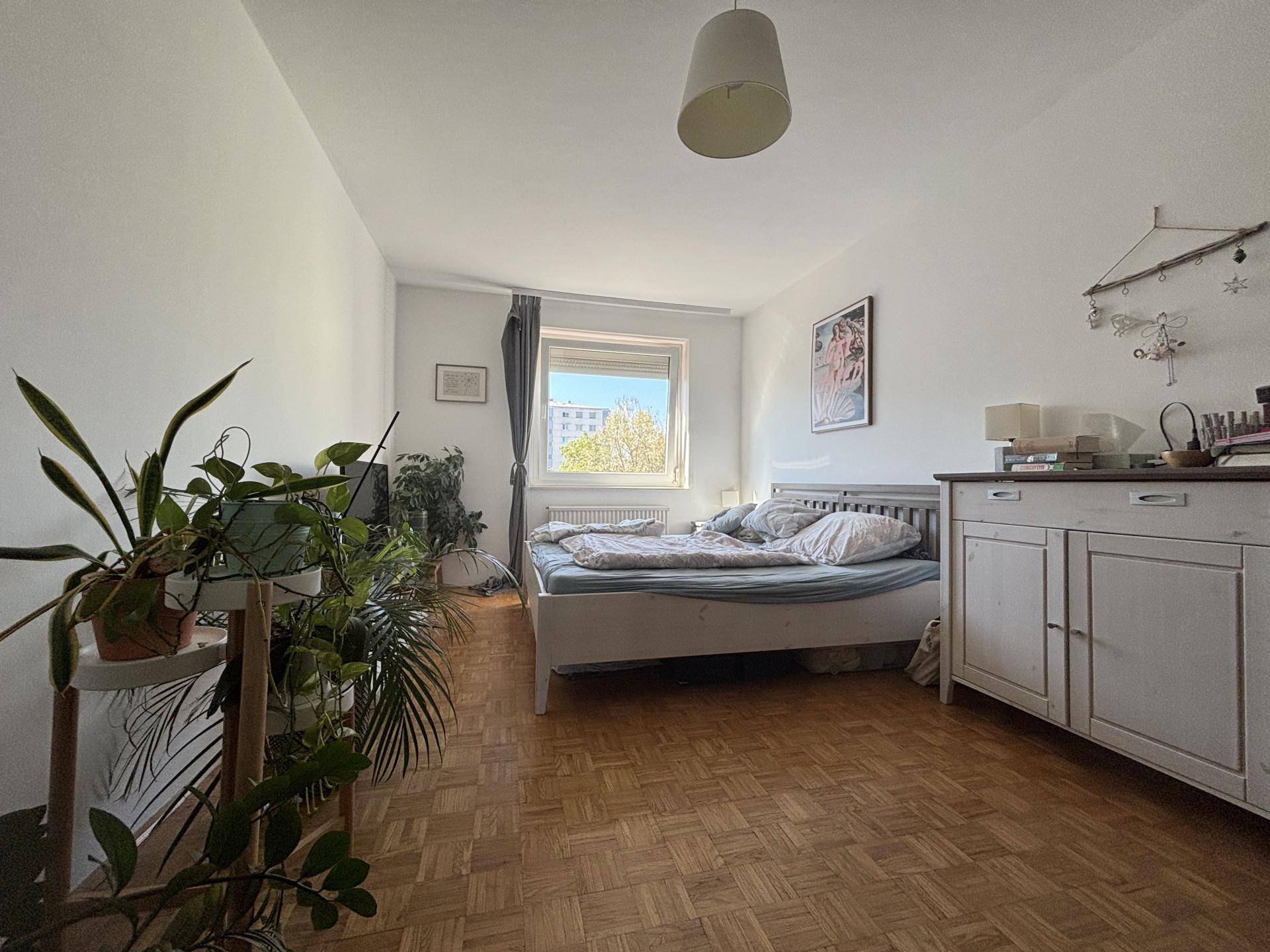 Helles Schlafzimmer mit Parkettboden, großem Bett und Pflanzen, bietet eine ruhige Atmosphäre.