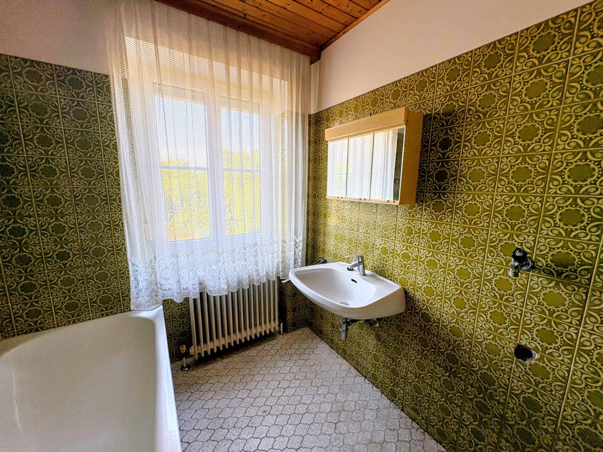 Badezimmer mit auffälligen grünen Fliesen, Badewanne, Waschbecken und Fenster für natürliches Licht.