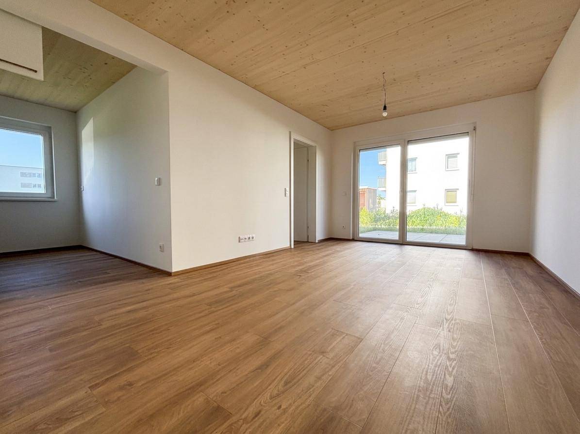 Heller, leerer Wohnraum mit Holzboden, Holzdecke und Zugang zu einem Außenbereich.