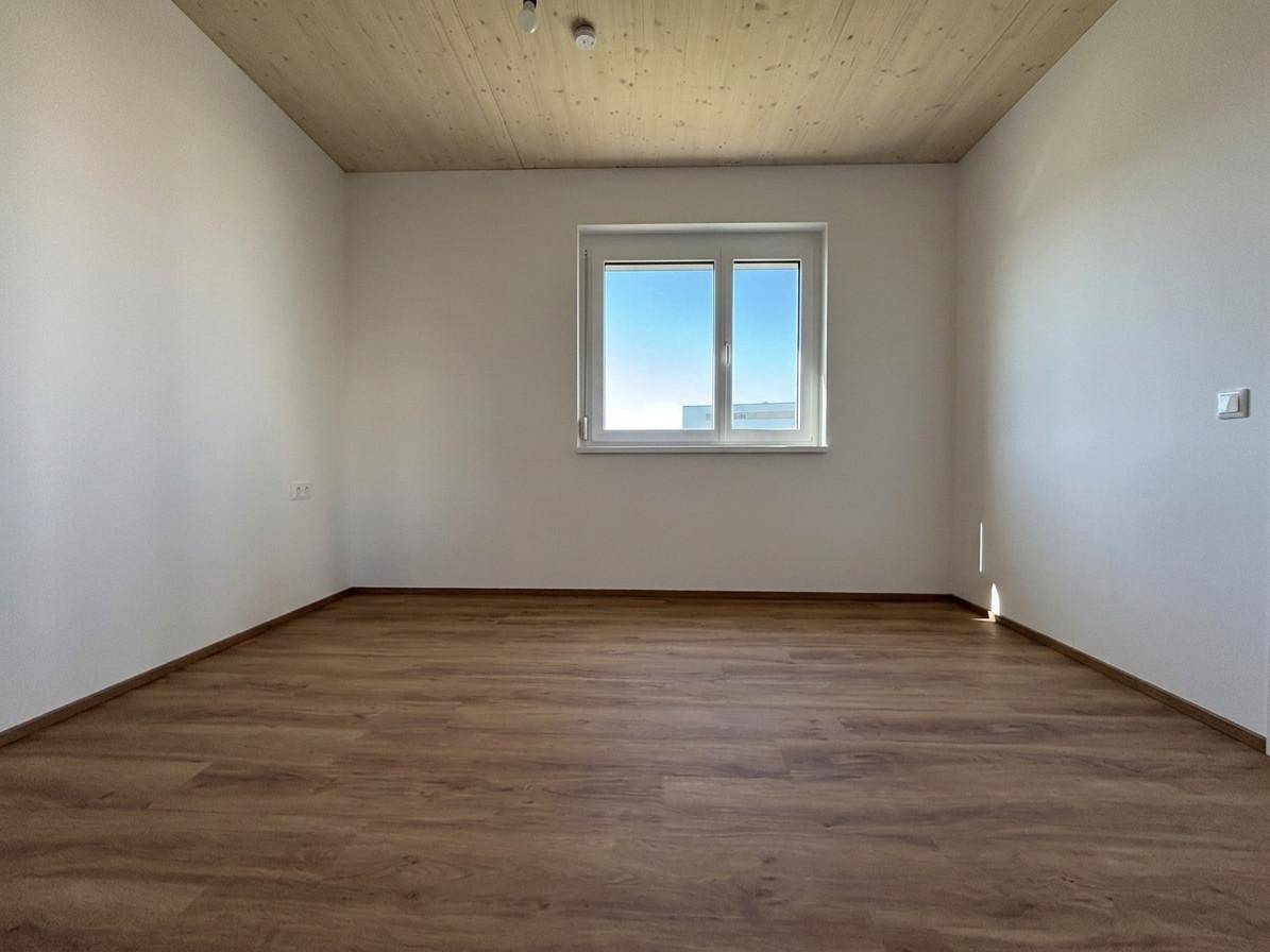Helles, leeres Schlafzimmer mit Holzboden, Holzdecke und großem Fenster.