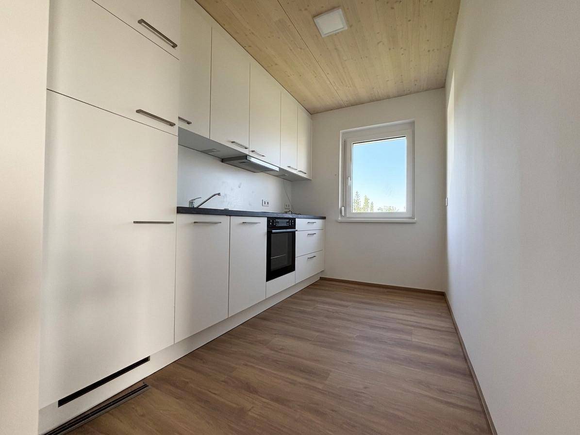Moderne, unmöblierte Küche mit weißen Schränken, schwarzer Arbeitsplatte und integriertem Backofen.