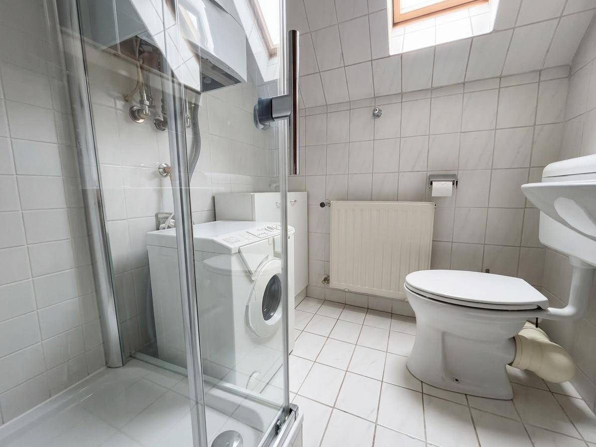 Badezimmer mit Dusche, Toilette, Waschmaschine und Dachfenster in hellen Fliesen.
