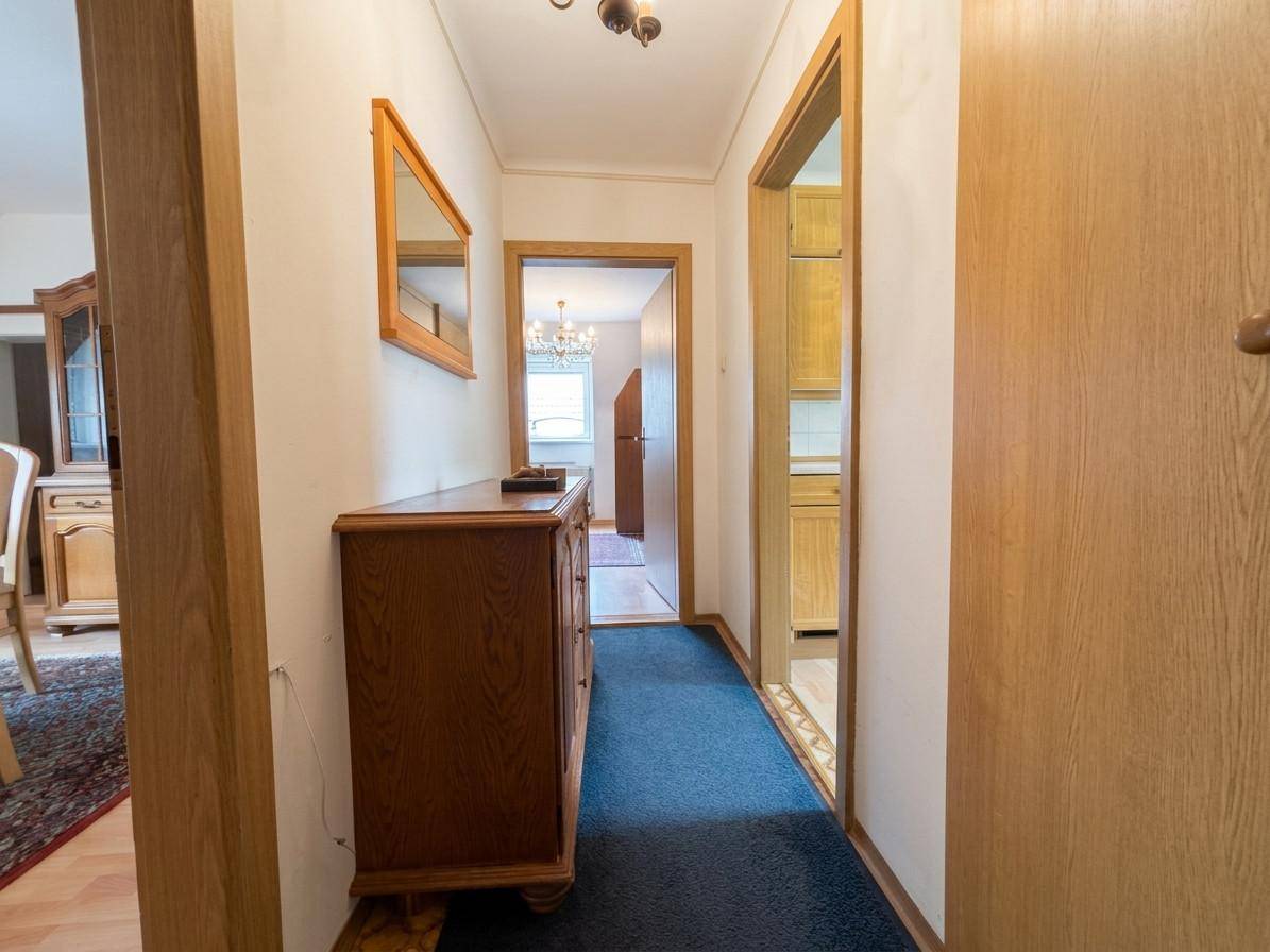 Flur mit Teppichboden, Kommode und Zugang zu weiteren Räumen mit Holztüren.