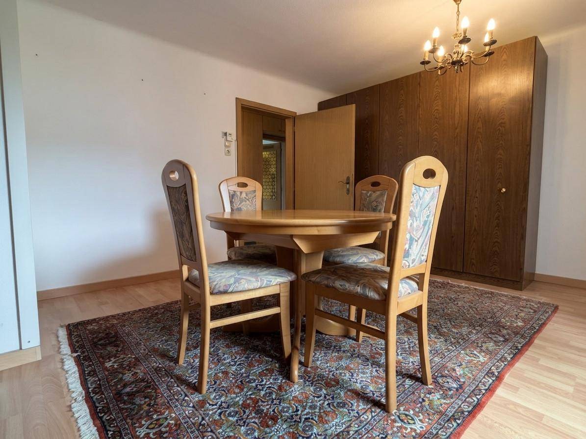 Essbereich mit Holztisch, Stühlen und einem großen Holzschrank in einem hellen Raum.