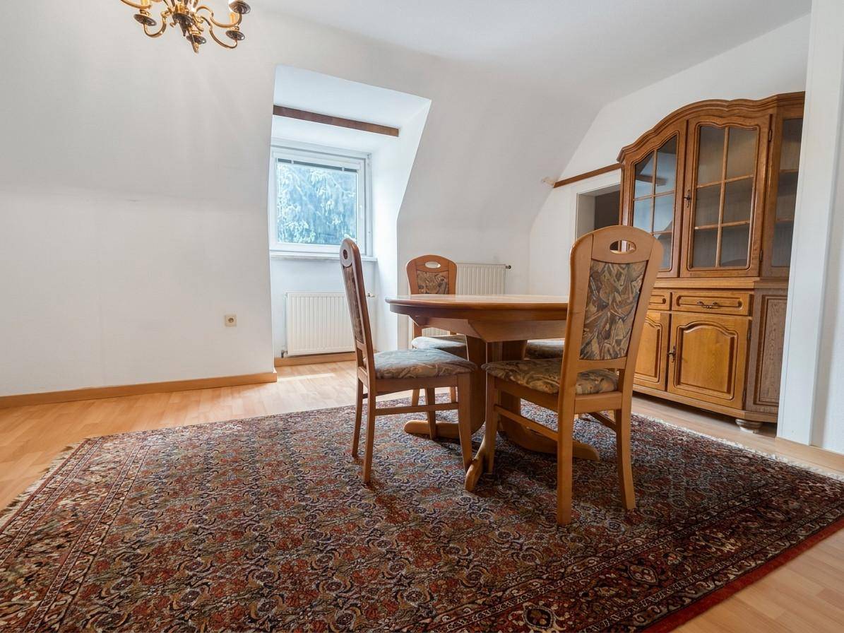 Gemütlicher Essbereich mit Holztisch, Stühlen und einem traditionellen Schrank auf einem Teppich.
