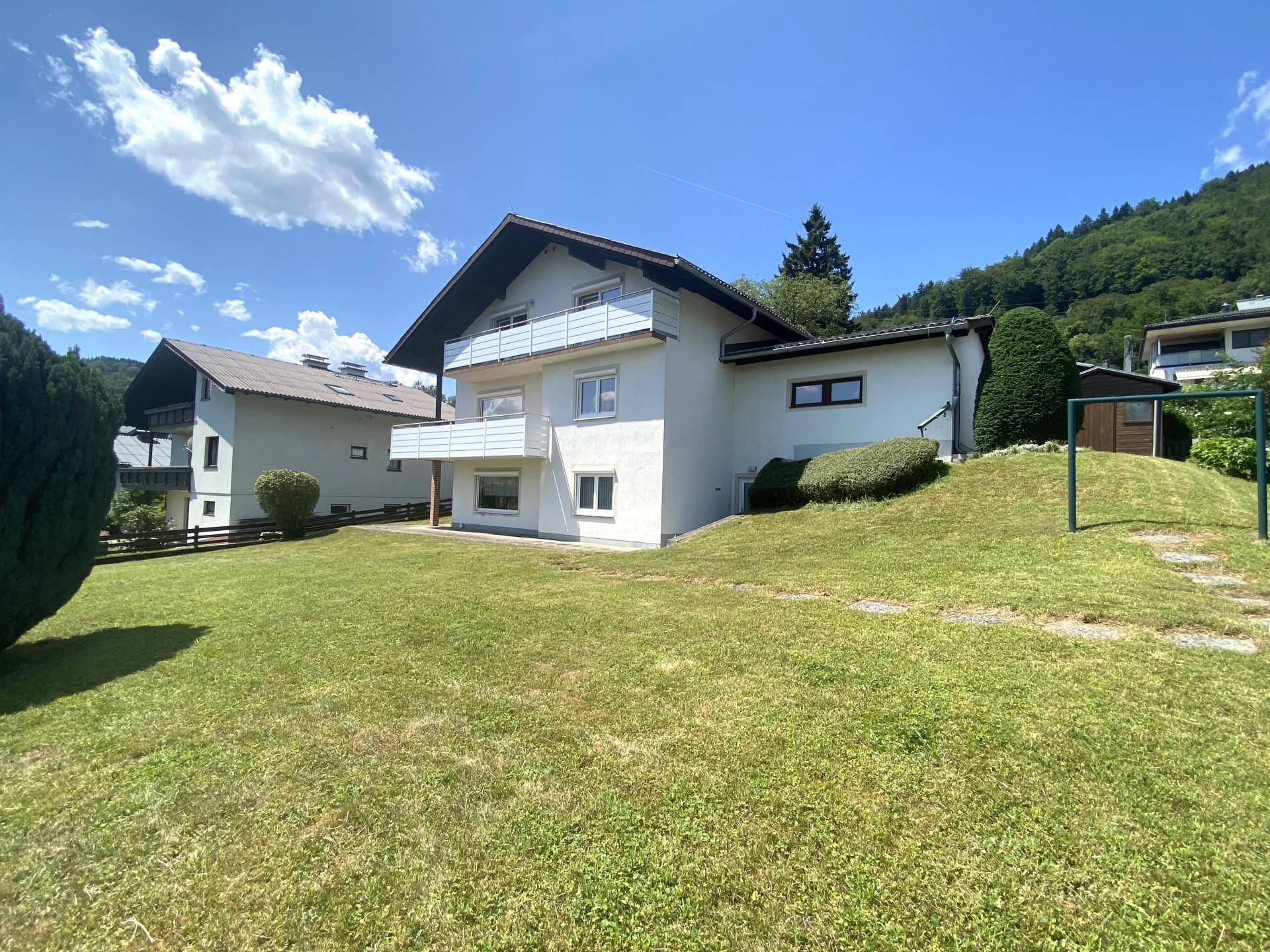 Rückansicht des Hauses mit großem Rasenbereich und Blick auf die bewaldeten Hügel.