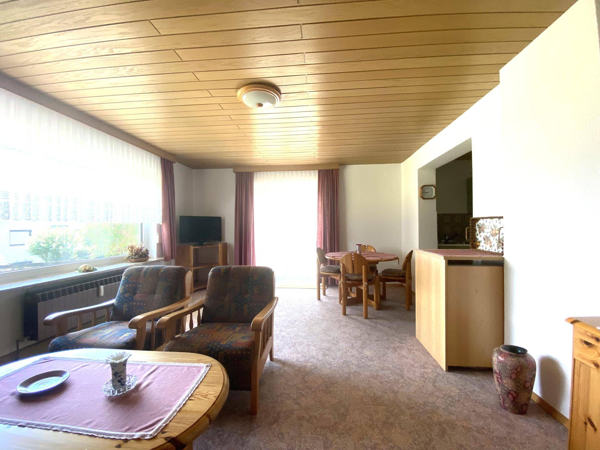 Gemütlicher Wohn- und Essbereich mit Teppichboden, Holzdecke und traditionellen Möbeln.