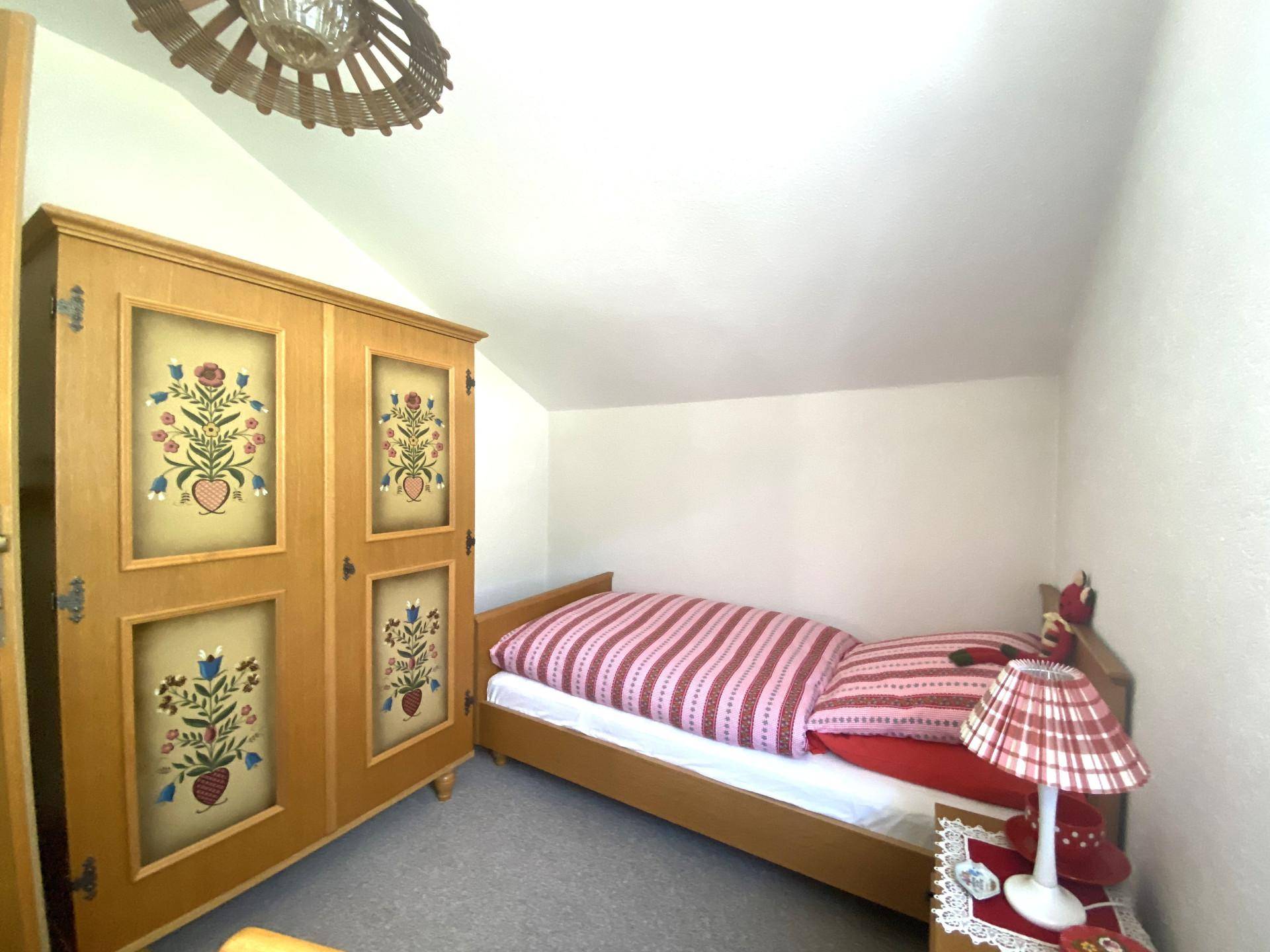Kleines Schlafzimmer mit Einzelbett, traditionellem Kleiderschrank und Dachschräge.