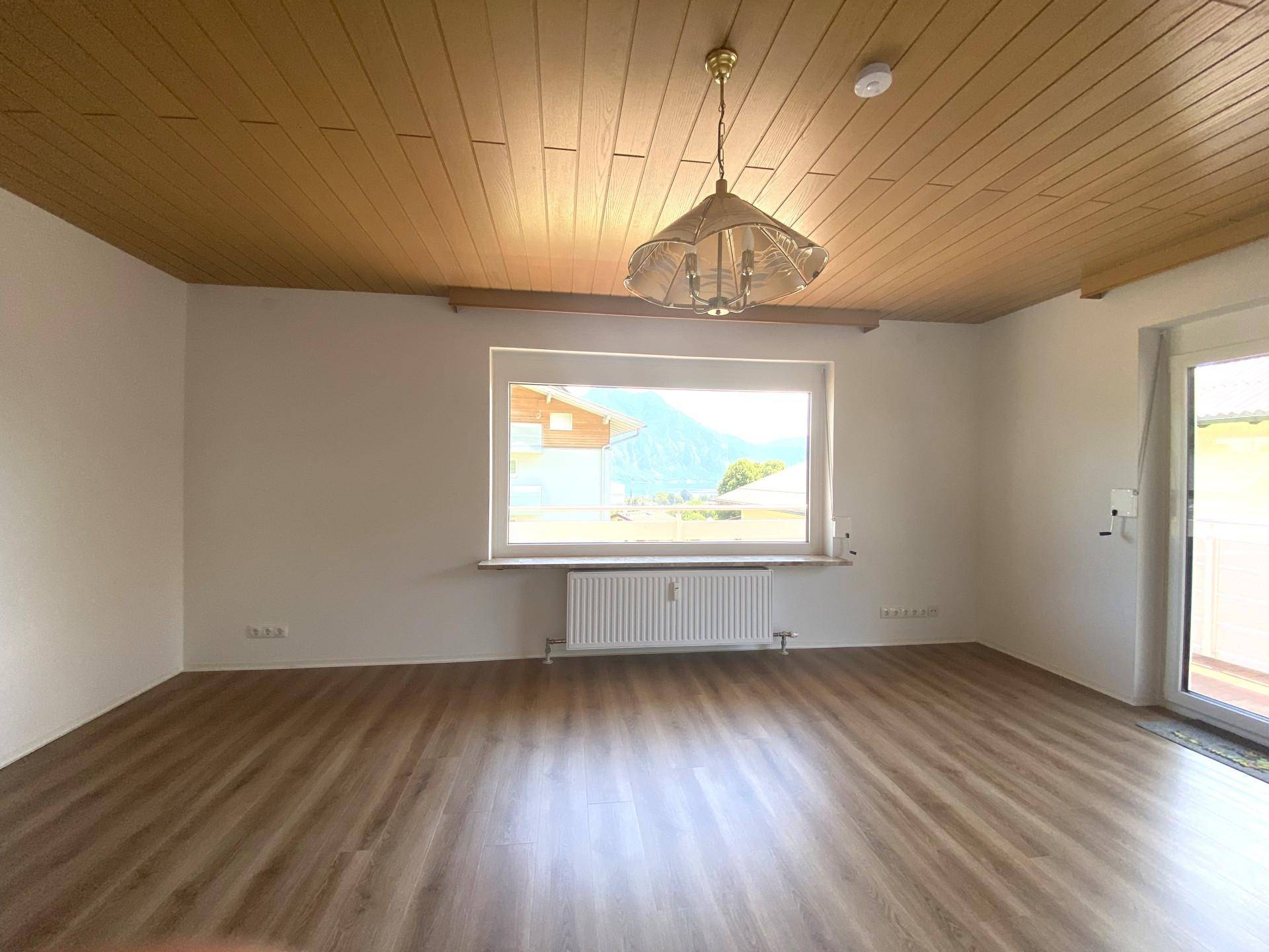 Heller, leerer Raum mit Laminatboden, Holzdecke und großem Fenster mit Bergblick.