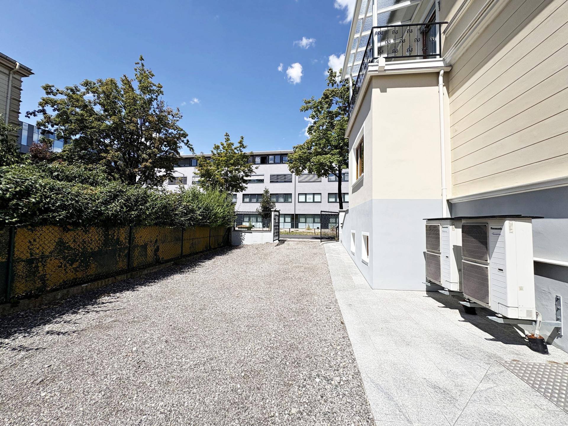 Seitenansicht des Gebäudes mit Kiesfläche und Klimaanlagen-Außengeräten unter einem Balkon.