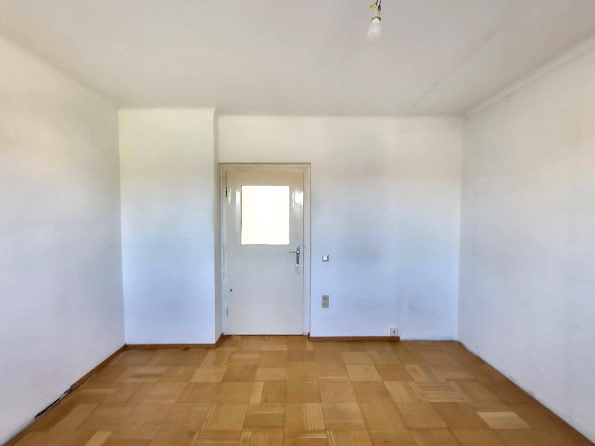 Unmöblierter Raum mit Parkettboden und einer Tür, die Tageslicht hereinlässt, ideal für individuelle Einrichtung.