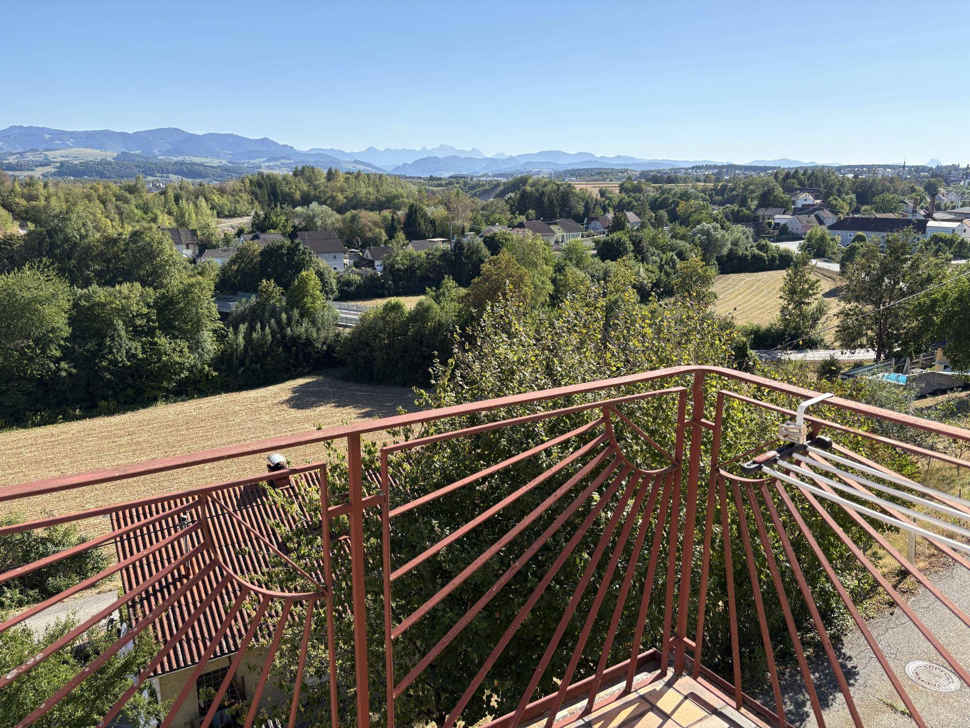 Weitläufiger Ausblick vom Balkon über Felder, Wälder und ferne Berge unter klarem Himmel.