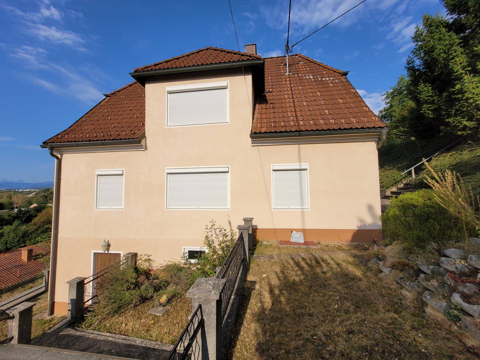 Frontansicht des Hauses mit geschlossenen Rollläden und einem leicht abfallenden Vorgartenbereich.